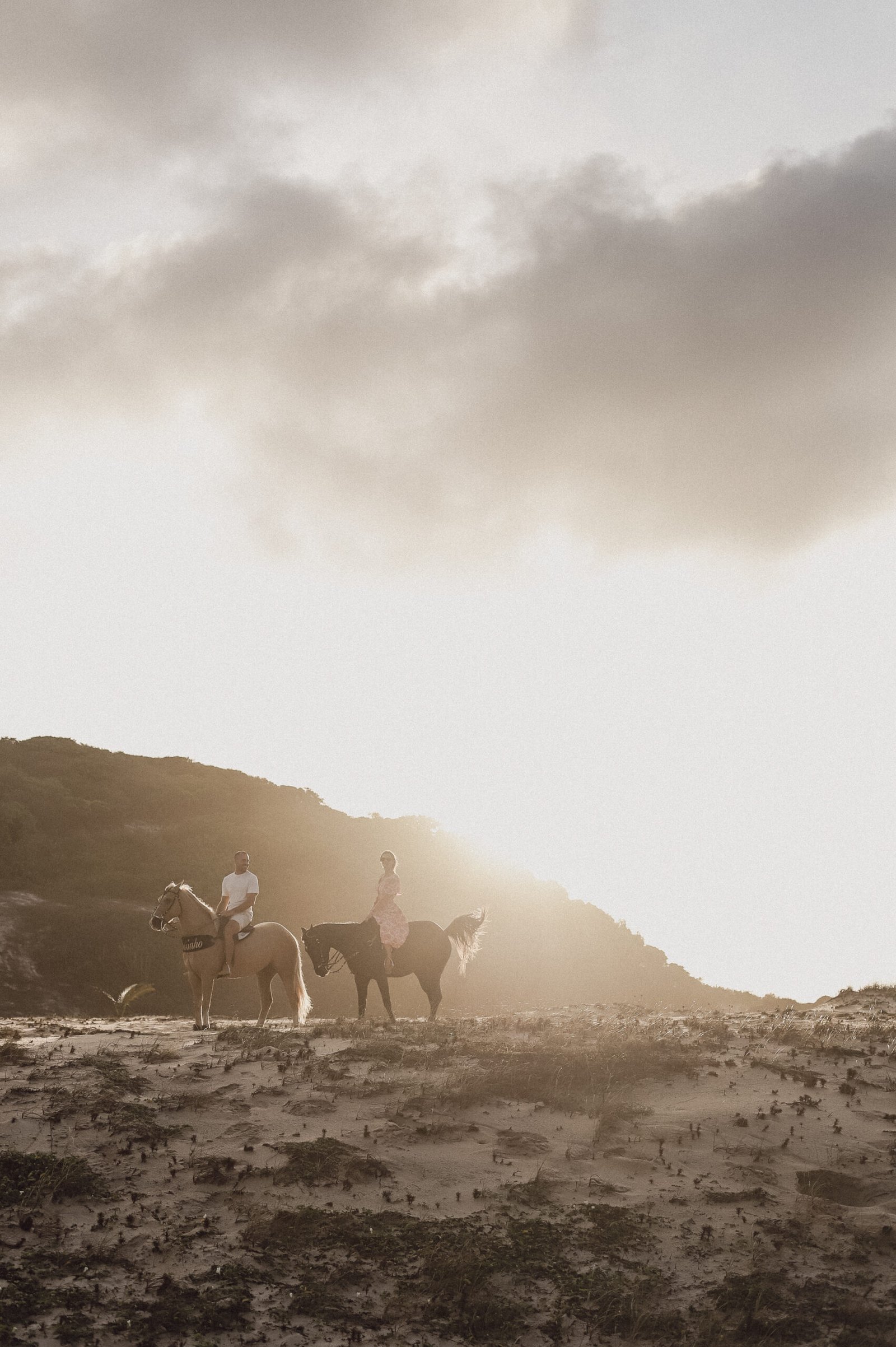 Duas pessoas a cavalo na praia ao pôr do sol