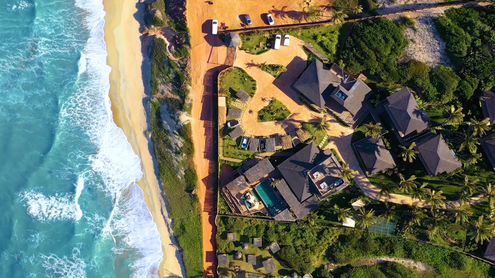 Vista aérea dos bangalôs de telhado de palha, piscina e o mar turquesa da Praia das Minas