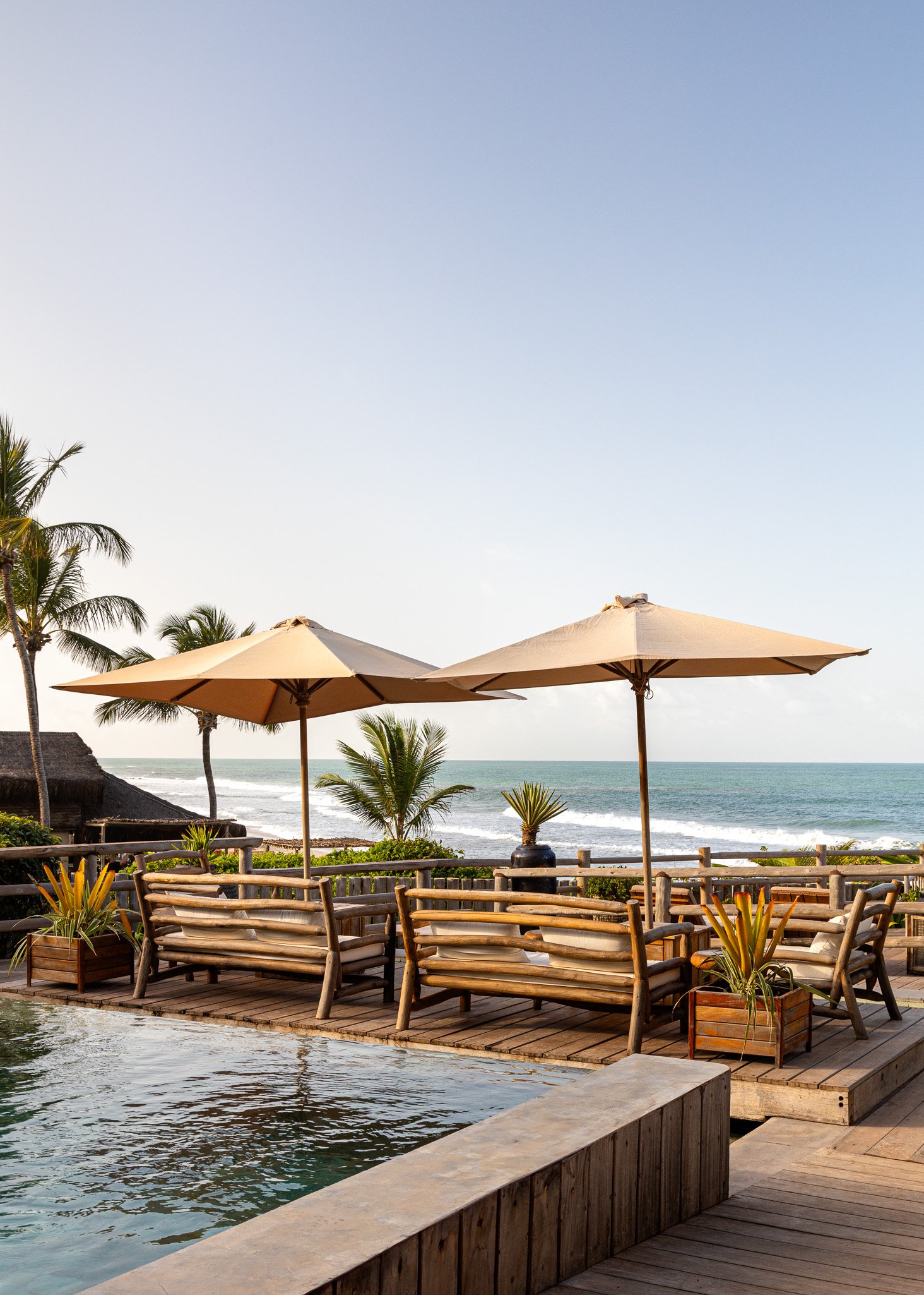 Deck de madeira com espreguiçadeiras e guarda-sóis à beira da piscina, com vista para o mar